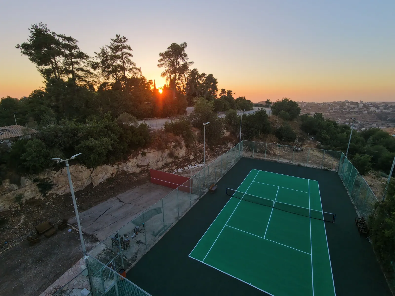מגרש טניס ירוק מול נוף הרי ירושלים בשעת הזהב